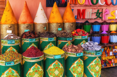 An array of Moroccan pantry essentials, including spices like cumin, coriander, and saffron, preserved lemons, olives, chickpeas, and various grains such as couscous and semolina, showcasing the vibrant ingredients commonly used in Moroccan cooking