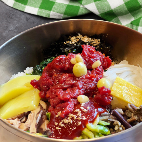 A colorful bowl of South Korean Bibimbap with brown rice, sautéed vegetables, tofu, and gochujang sauce.